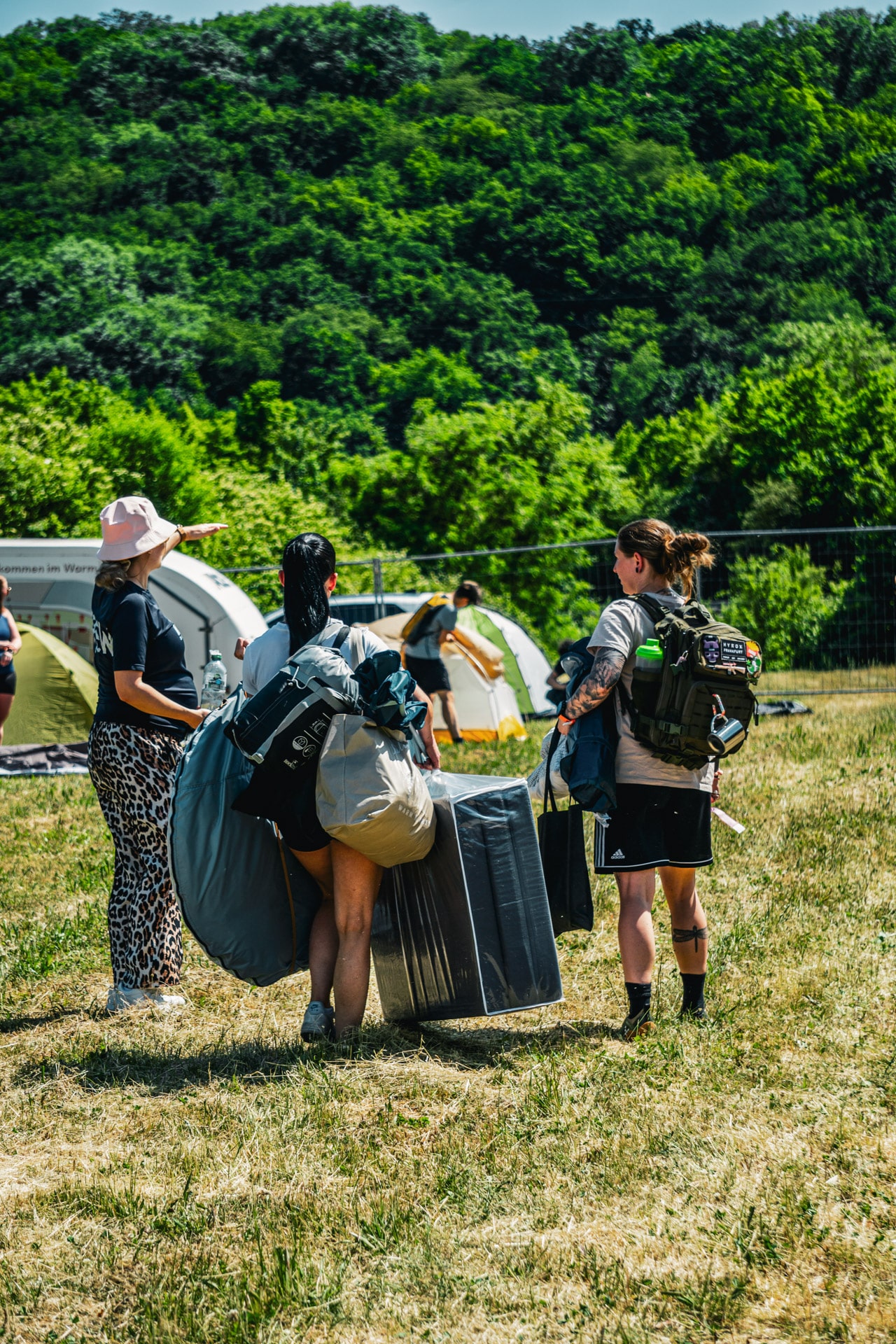 Teilnehmerinnen tragen ihr Gepäck beim Check-in über die Zeltwiese des Bootcamps
