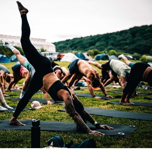Gruppe übt Yoga auf Matten im Gras, im Hintergrund Zelte