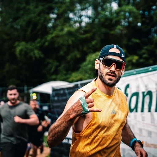 Läufer mit Sonnenbrille, Basecap und gelbem Trikot im Freien vor einem Banner