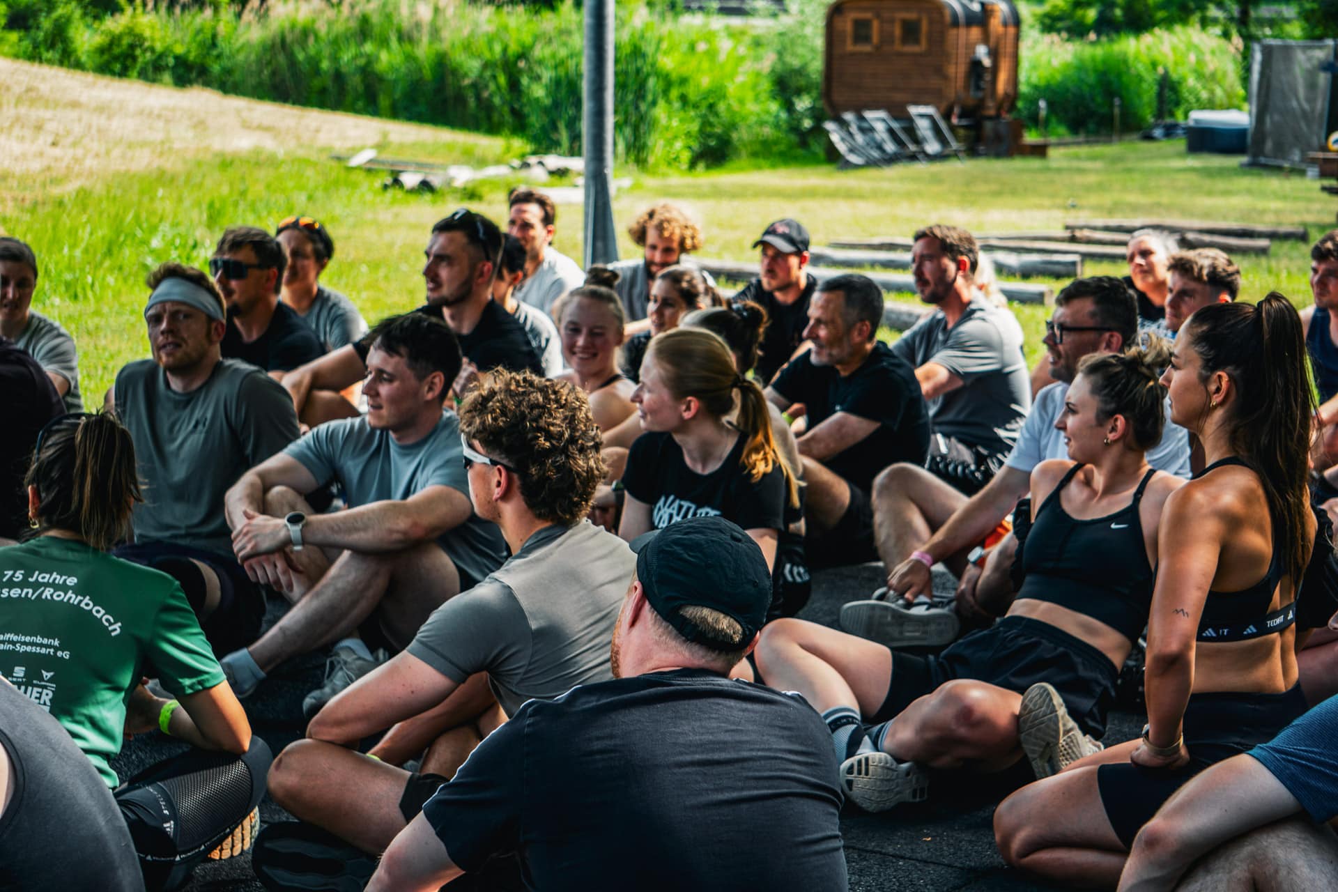 Teilnehmer des Nature Warriors Bootcamps sitzen entspannt zusammen auf dem Eventgelände