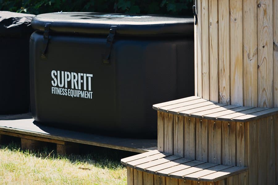 Eine schwarze, eckige Eiswanne mit SUPRFIT-Logo neben einer Holztreppe auf der Wiese